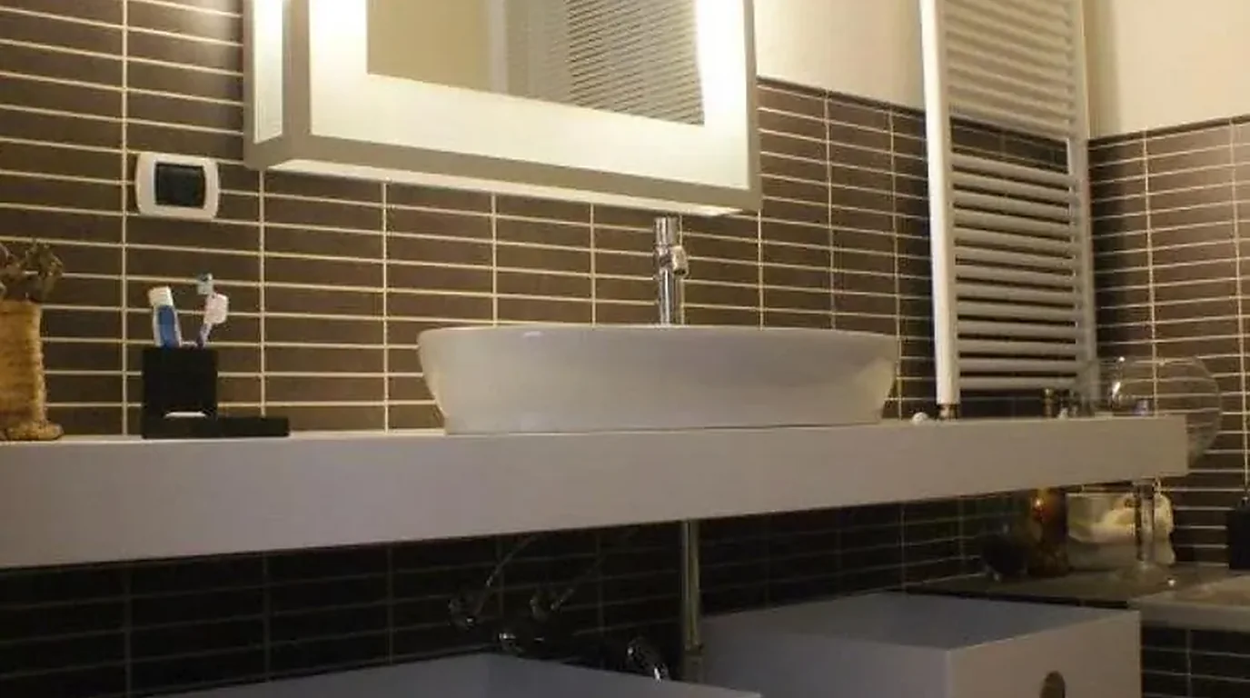 Baño reformado con alicatado oscuro, lavabo sobre encimera y toallero
