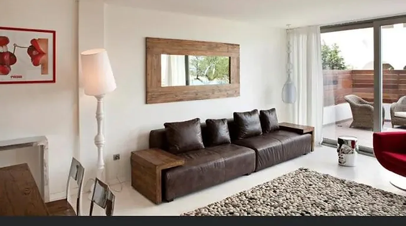 Salón reformado con sofá de piel, espejo y terraza en una vivienda de Paterna
